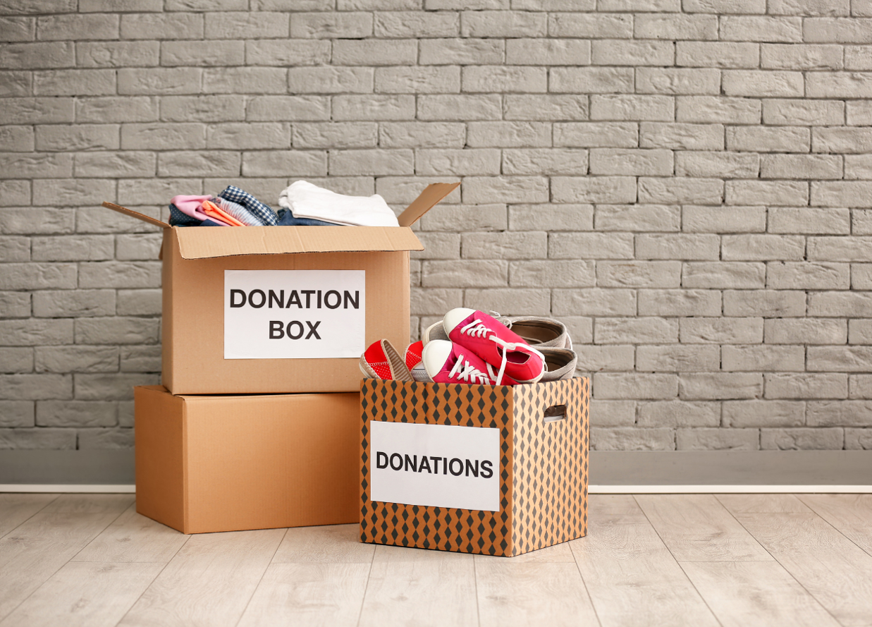 Donation boxes with clothes and shoes on the floor against a brick wall